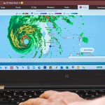 The laptop monitor screen shows Hurricane Ian Category 4, the radar eye belt of the Gulf of Mexico, close to the landing of Miami Beach, Florida.