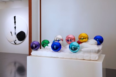 A sleeping nude sculpture with polished colored balls in the foreground, black and white circular abstract painting hanging on the wall on the background. 