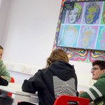 Four students show off art under the screen.