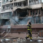 Burning building with smoke, a man in black and yellow protective suit.
