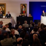 Scene in the auction: One person stands on a podium, next to a few people.