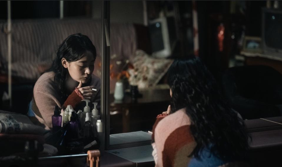 A young woman smoking in front of a mirror.