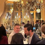 Several people stood around the bar, illuminated by a golden chandelier.