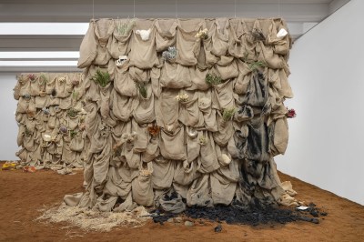 The two towers feature rows of trouble sacks that hold various objects, including dried flowers and feathers. One area is coated with a black grey substance. Plant the tower in a dirt-covered ground.