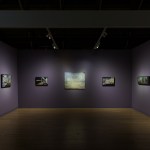 An art fair stall with purple walls and several New York City landscape paintings on it.