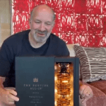 A man is holding a bottle of tequila on the sofa. Behind the sofa is a curly red face.