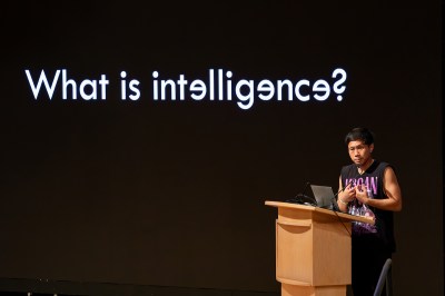 A man on the podium under a projection reading 