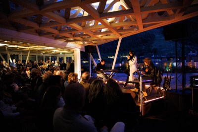 A woman on stage with two band members and an audience in front of her.