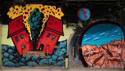The mural shows a house, one divided into two parts, with clouds rising, a globe and a portal with a cattle body.