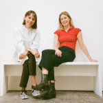 Two smiling women sitting on bench.