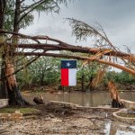 Texas Central Point - July 13: A storm-damaged tree on the banks of the Guadalupe River flies a Texas flag on July 13, 2025 at Texas Central Point. More than 160 people are still missing after the storm cell parked in the area, dumped nearly 15 inches of rain and rose 22 feet above the Guadalupe River. (Photo taken by Brandon Bell/Getty