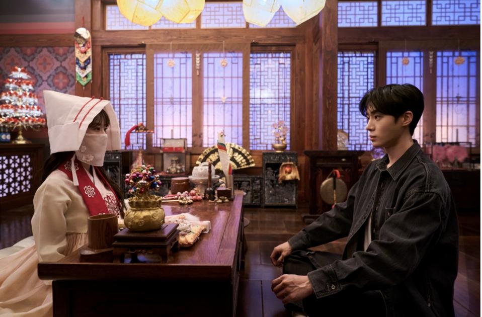 A young man wearing a mask sitting in front of a shaman.
