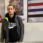 A man in a hoodie stands in front of three posters.