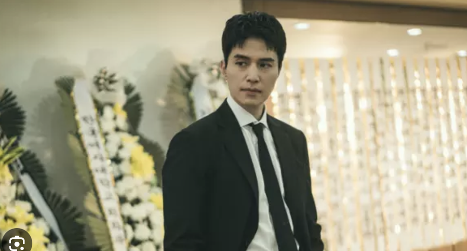 A man in a black suit stands in a funeral hall in South Korea.