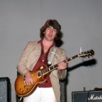 A man holding a guitar in front of an amplifier.