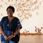 Smiling black woman in a blue shirt standing in front of art installation.