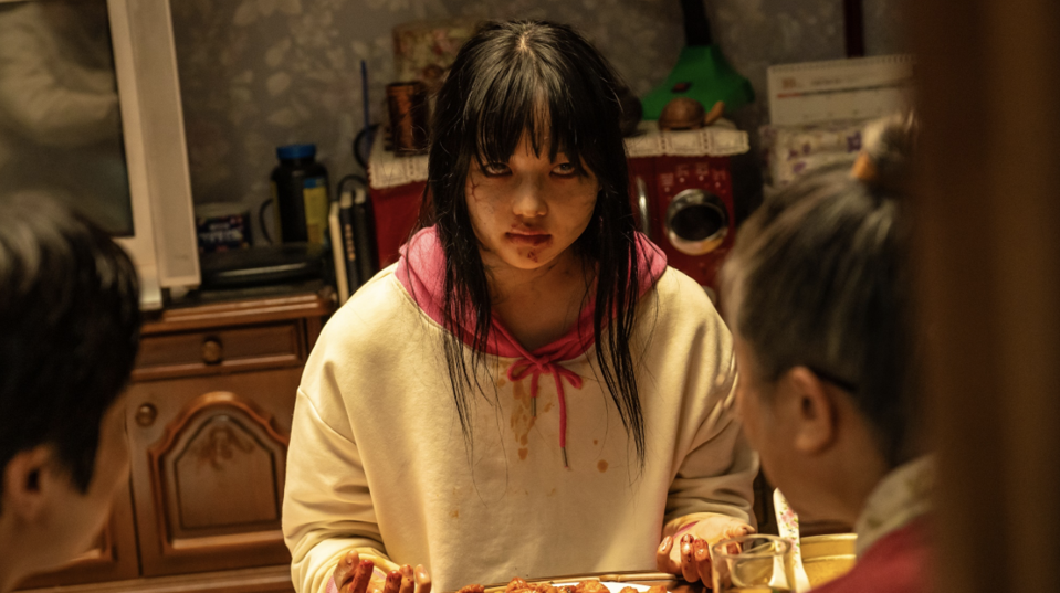 A teenage girl zombie sits down and eats a human meal.