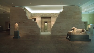 A dimly lit gallery with a bricked building and two sculptures in front of it.