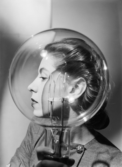 A woman standing beside a large light bulb.