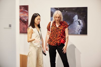 Two women discuss invisible works (on the floor) at the art fair. 