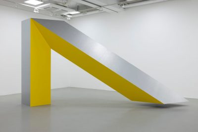A steel sculpture resembles a large inverted V with a yellow painted side.