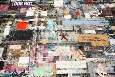 A detail of a sculpture made of wiring on various dozens of scrap of fabric and other materials have been tied to it.
