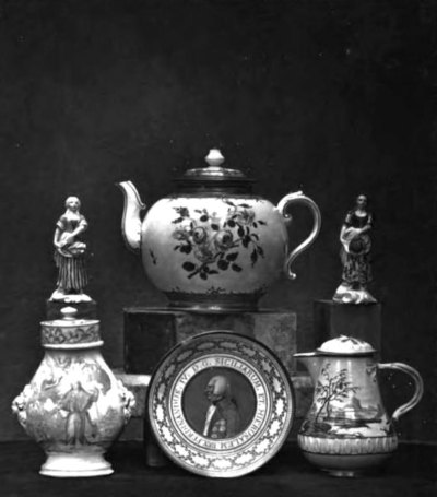 An archival image showing various ceramics, including a teapot, a pitcher, a plate, and figures. 