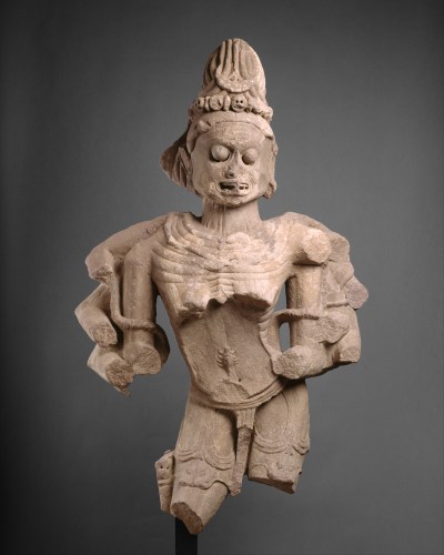 An aged sculpture of a sharp-toothed person with broken arms and legs and bulging eyes.