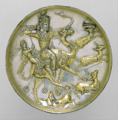 A plate showing a man on a bull shooting arrows at gazelles while a woman rides in tow. The silver plate is sculpted so that gold areas pop out of its surface.