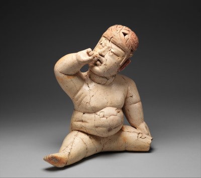 A sculpture of a figure with a fat stomach and splayed legs who holds one hand to their mouth. Cracks run through the sculpture.