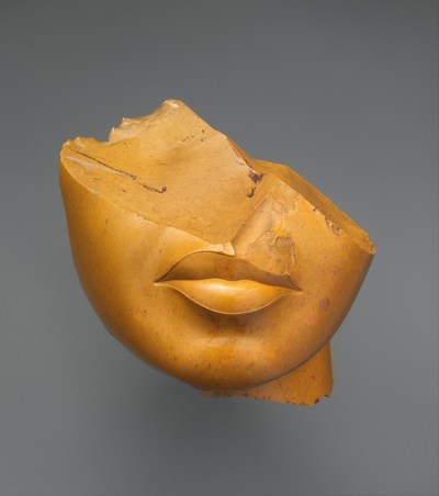 A yellow jasper sculpture of a woman's face that is broken so that her eyes are missing.