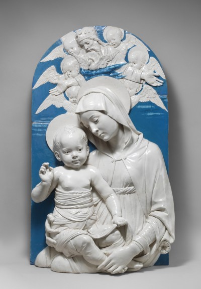 A sculpted image of a Virgin Mary holding a baby with angels overhead. The figures are left white, while the background behind them is glazed in a rich blue.