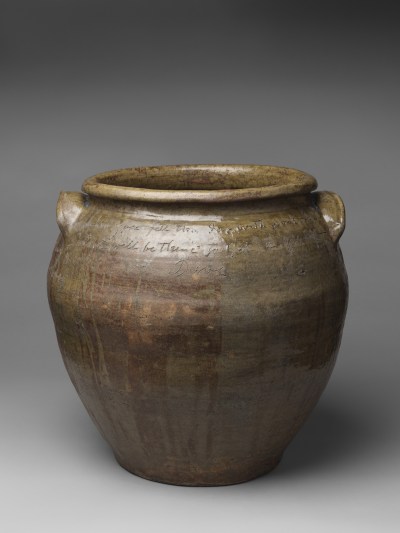 A glazed jar with unreadable writing scrawled into its surface.
