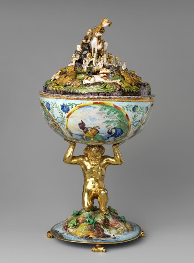 An ornate cup whose stem is made from a golden nude man. He kneels on an island with animals crawling around it and holds up the cup.