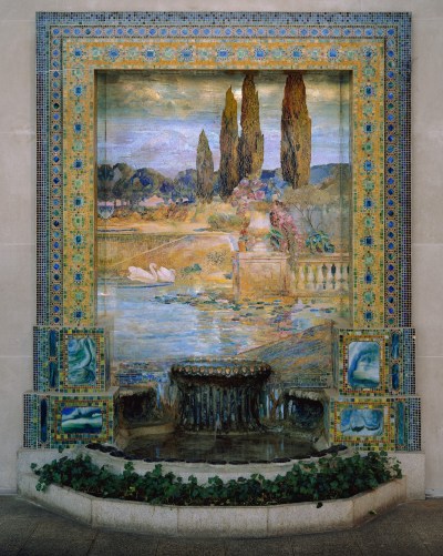 A fountain set within a large mosaic showing swans swimming through a lake beside a balcony and some cypresses.