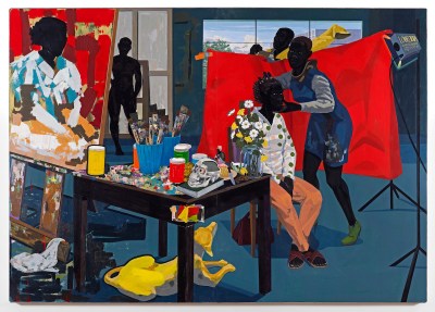 A painting of an artist's studio filled with Black assistants and models. One model sits in a chair while another poses him before a light and a red backdrop.