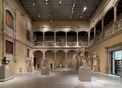 An open room with two levels of marble archways. On the floor are marble sculptures.