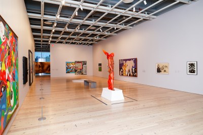 A gallery with paintings on its walls and a sculpture of a man on fire in its center.
