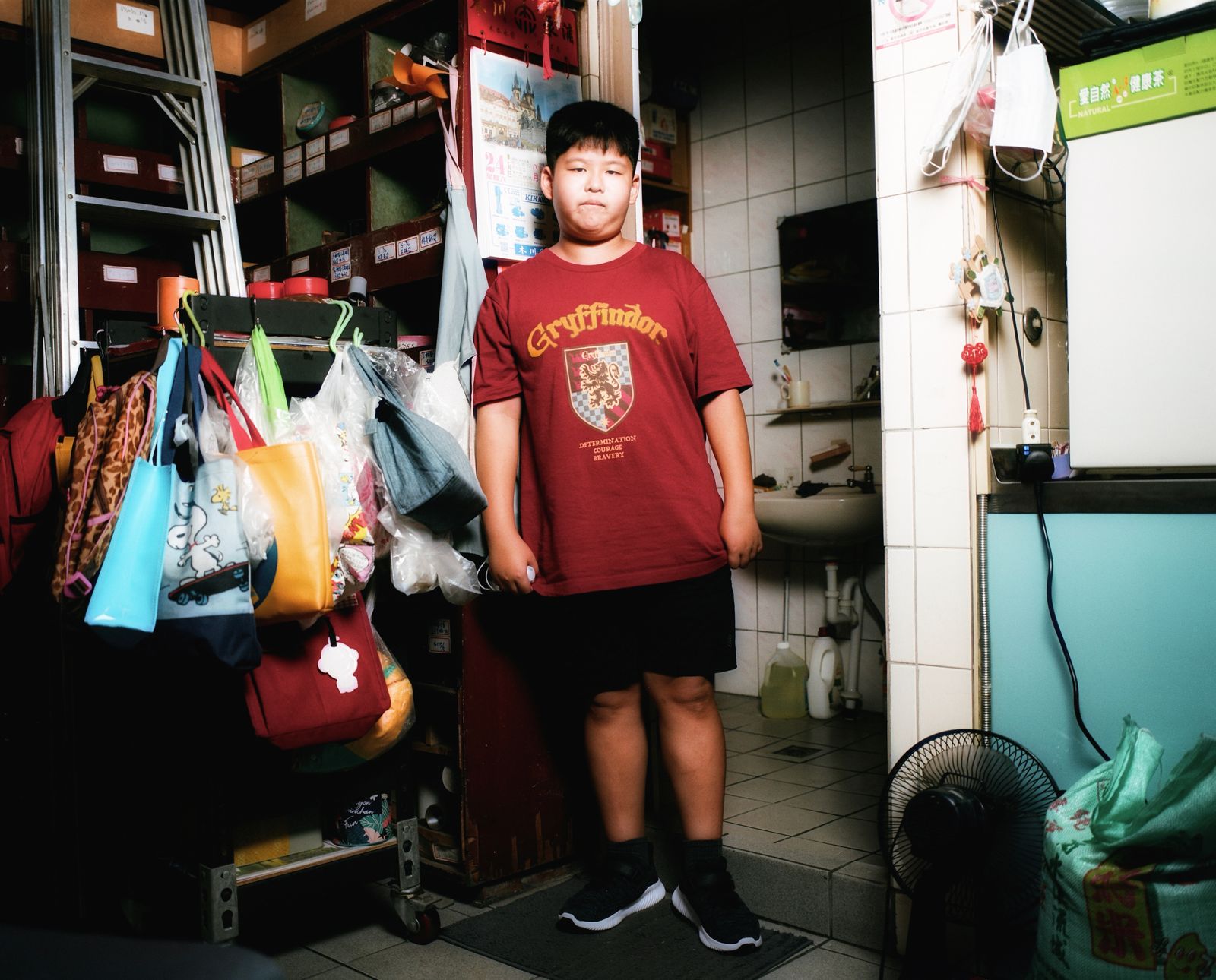 A boy stood in front of a bathroom in Taiwan, wearing a Gryffindor T-shirt reading. Behind him...