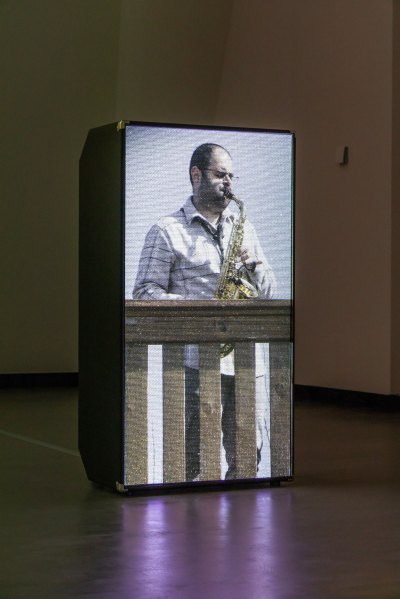 Vertical screen shows a man playing saxophone on the balcony. 