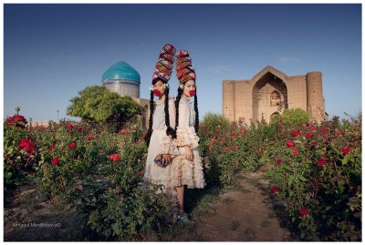 View of two traditional Kazakh women standing in a garden with buildings behind. 