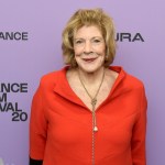 A woman in an orange dress on a red carpet.