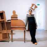 A woman leans against a sculpture combination partly composed of wooden tables.