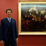 A man in a suit stands next to the painting.