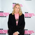 A woman stands on the red carpet, holding her hands tightly.