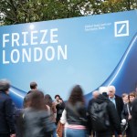 Fairgoers walk in front of the Frieze London sign.