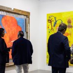 Four people read two paintings at an art fair.