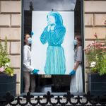 Two women holding a large female painting.