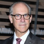 A white man wearing glasses smiles.