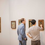 Two men admire a 20th century painting in a fancy frame.